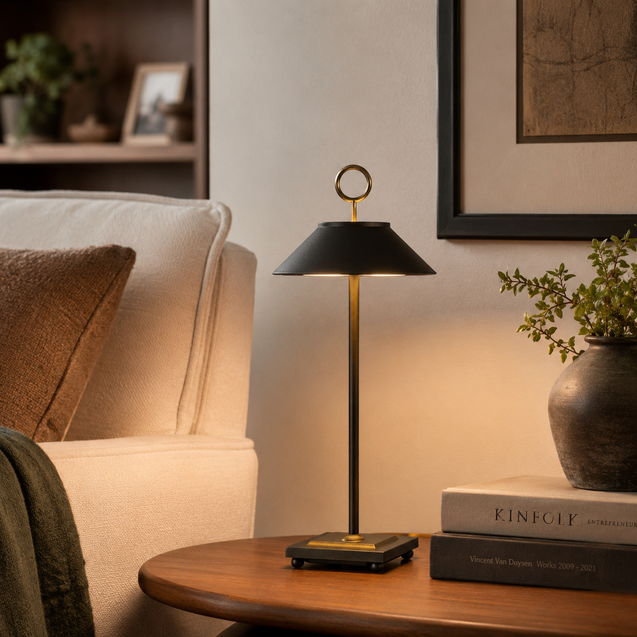 Eine moderne schwarze Lampe mit goldenen Akzenten steht auf einem Holztisch neben Büchern und einer Vase.