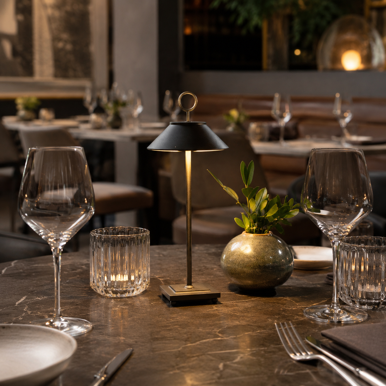 Ein Tisch in einem Restaurant mit Gläsern, Lampe, Kerze und Vase.