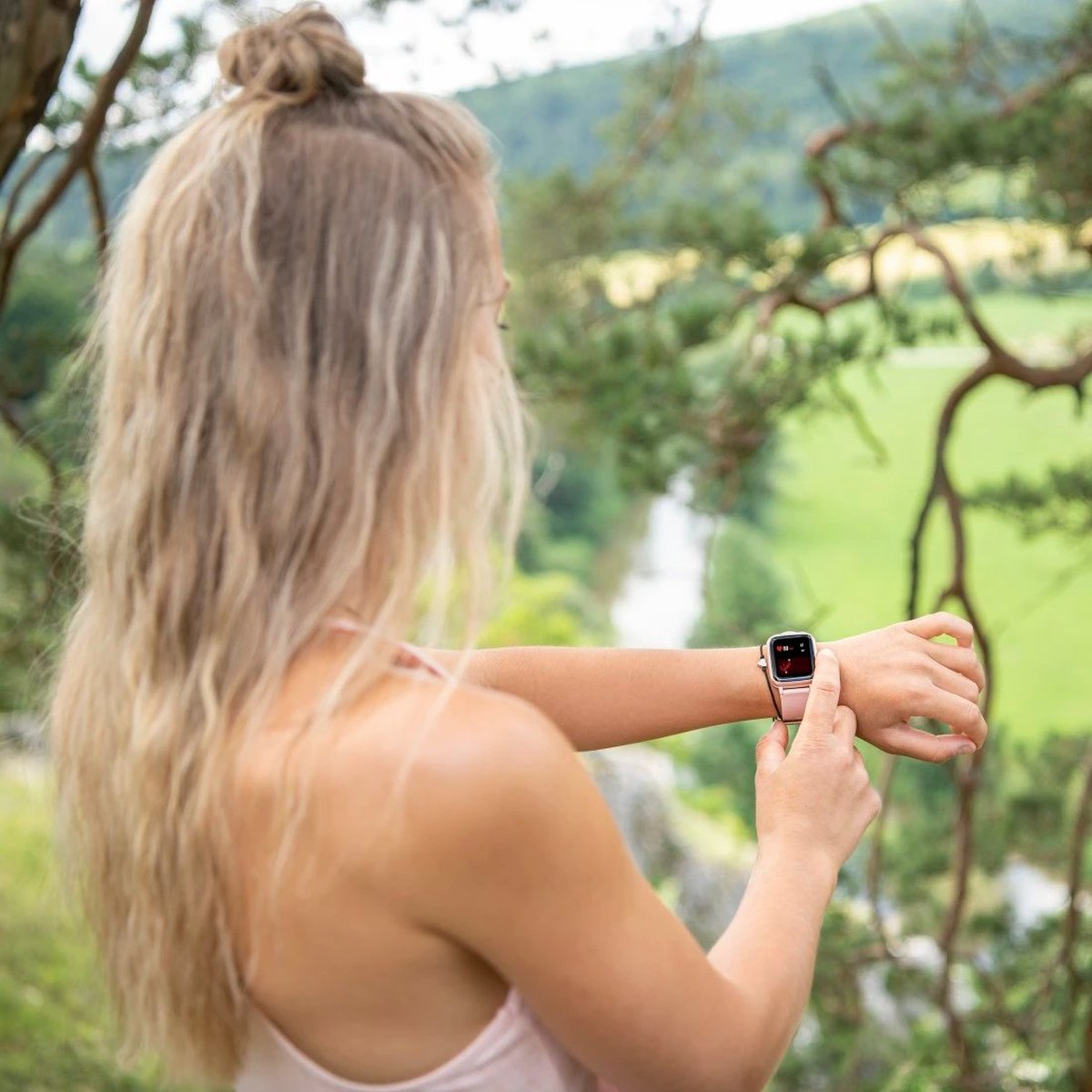 Una donna con uno chignon biondo controlla il suo smartwatch rosa all'aperto.