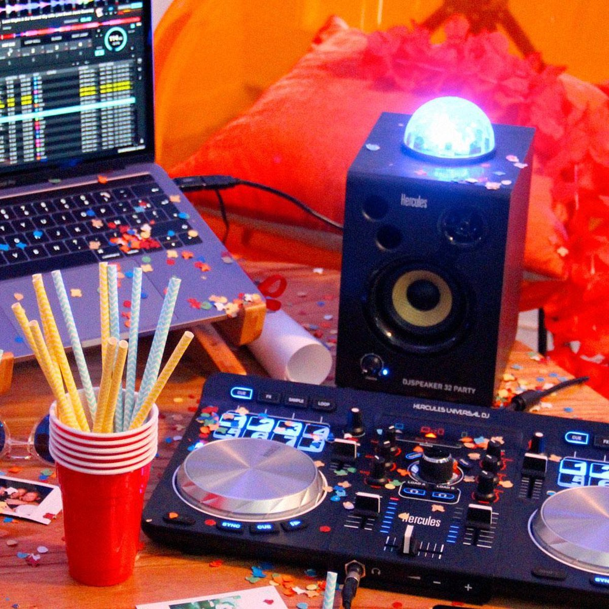 DJ-apparatuur met laptop, luidspreker, mixer, rode beker met rietjes, confetti.