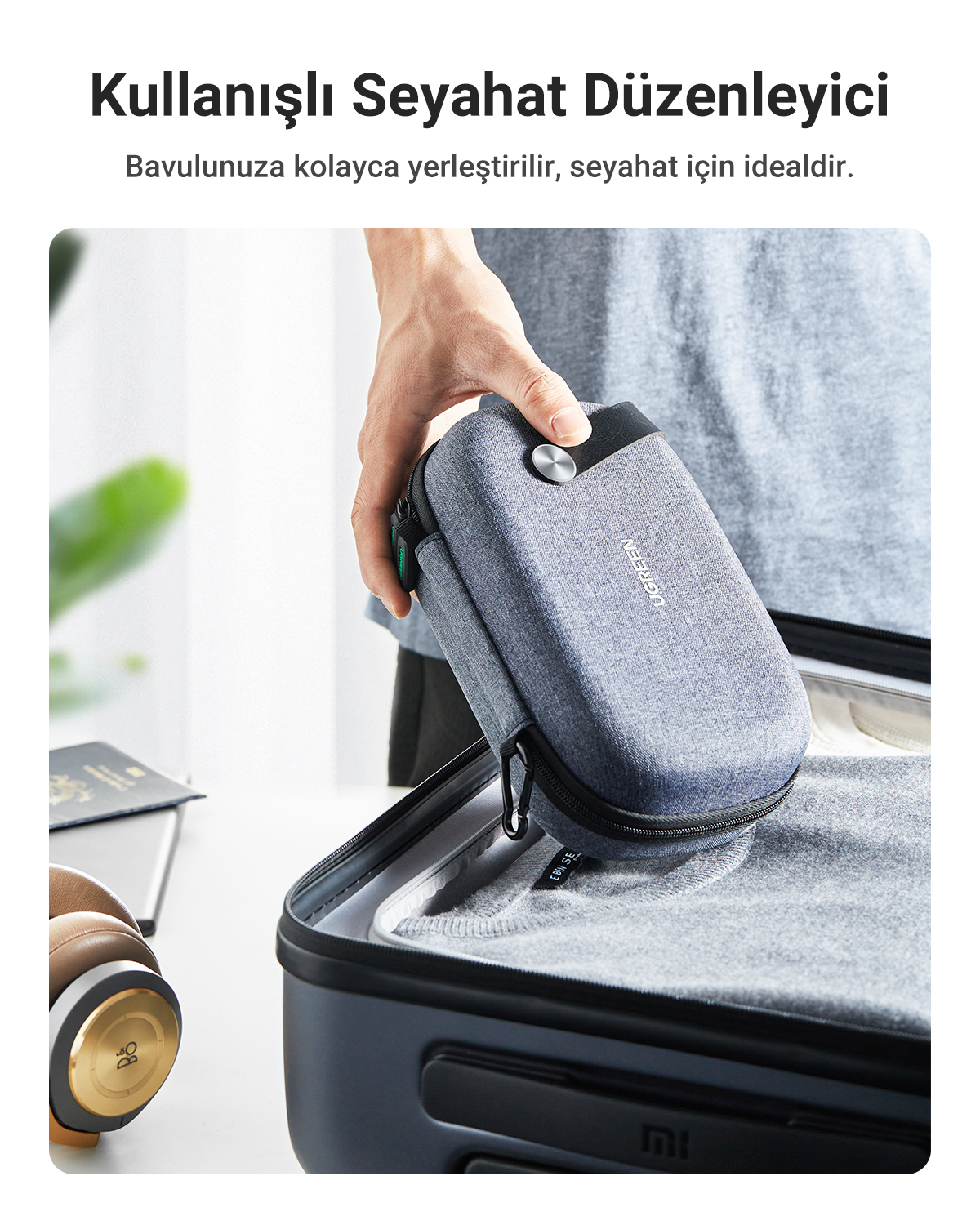 Eine Hand legt eine graue Reisetasche in einen Koffer. Kopfhörer liegen daneben.