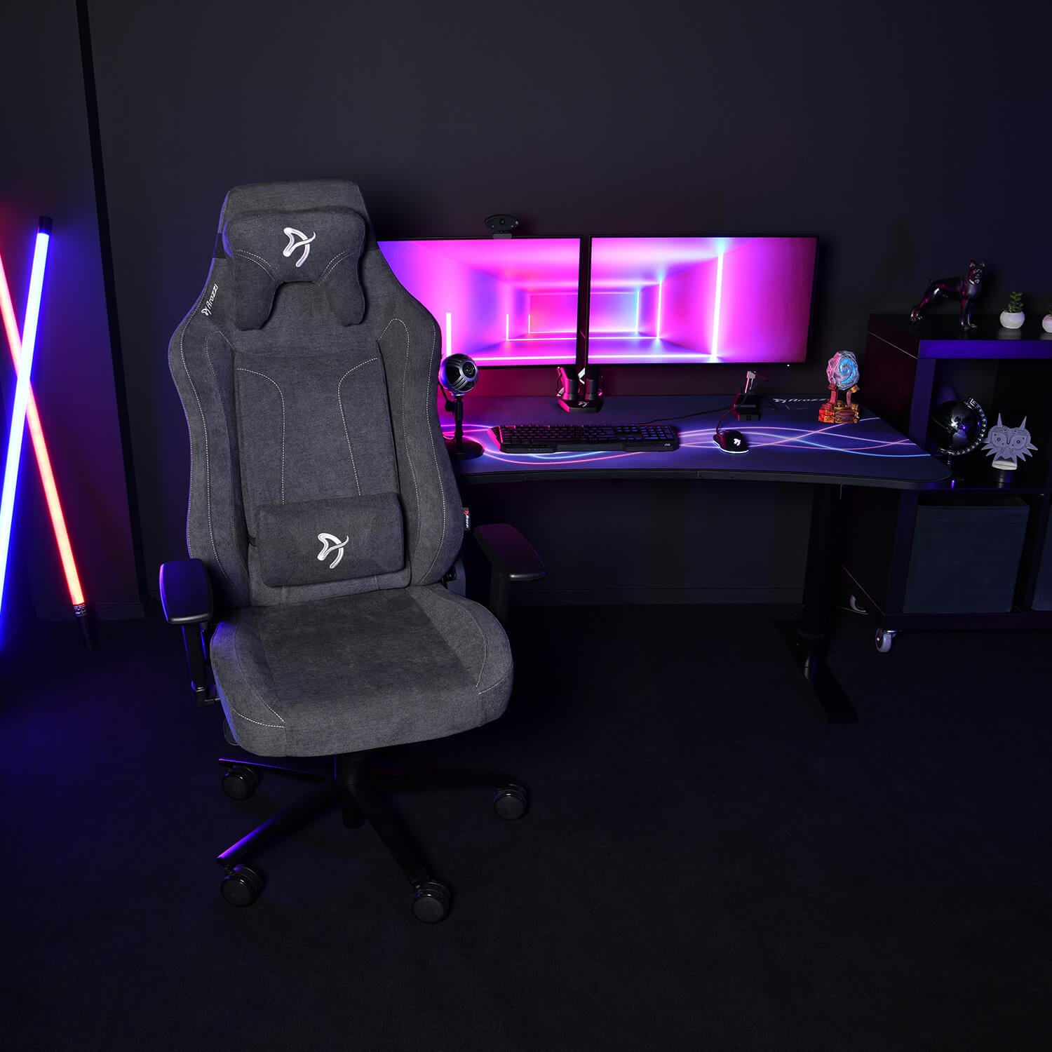 Een donkergrijze gamestoel staat voor een bureau met dubbele monitoren die neonverlichting tonen.