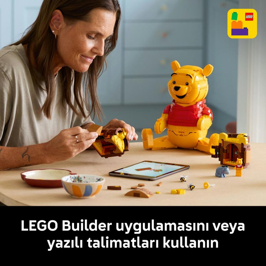 Kadın Winnie the Pooh LEGO inşa ediyor. Tablet talimatları gösteriyor. Arı ve eşek figürleri.