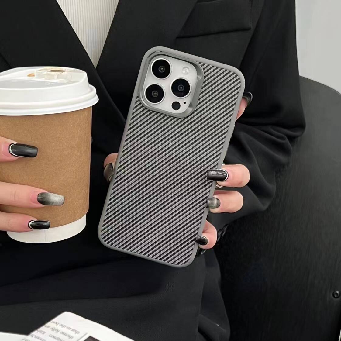 Kişi karbon desenli kılıflı bir akıllı telefon ve kahve tutuyor.