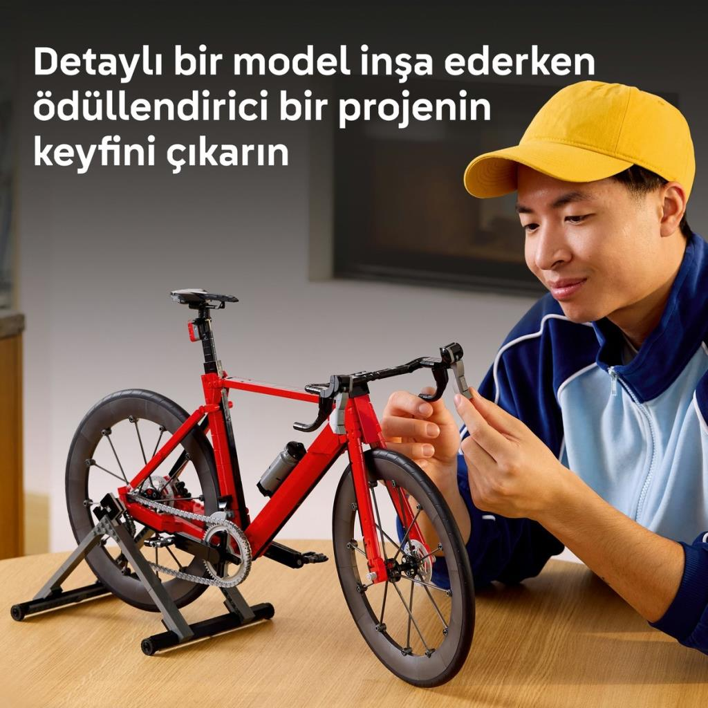 Sarı şapkalı adam masada kırmızı Lego bisiklet modeli inşa ediyor.