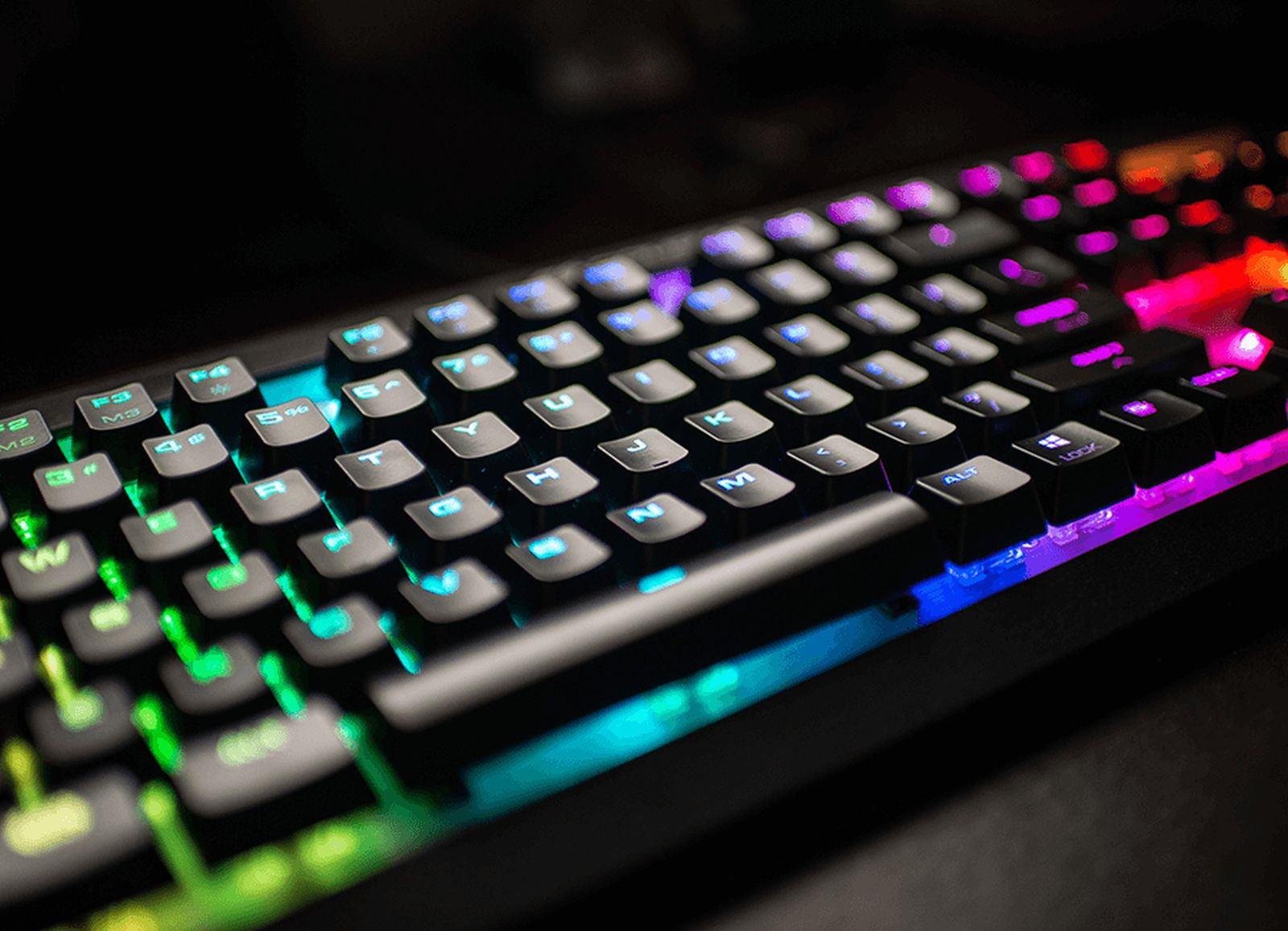 Nahaufnahme einer schwarzen mechanischen Tastatur mit lebendiger RGB-Hintergrundbeleuchtung in Grün, Blau, Lila und Rot.