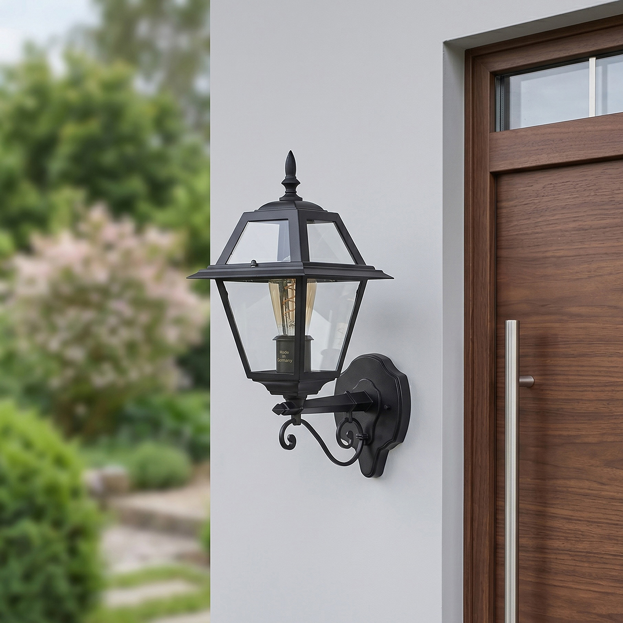 Eine schwarze Außenlaterne mit Glasscheiben ist neben einer Holztür an einer weißen Wand montiert.