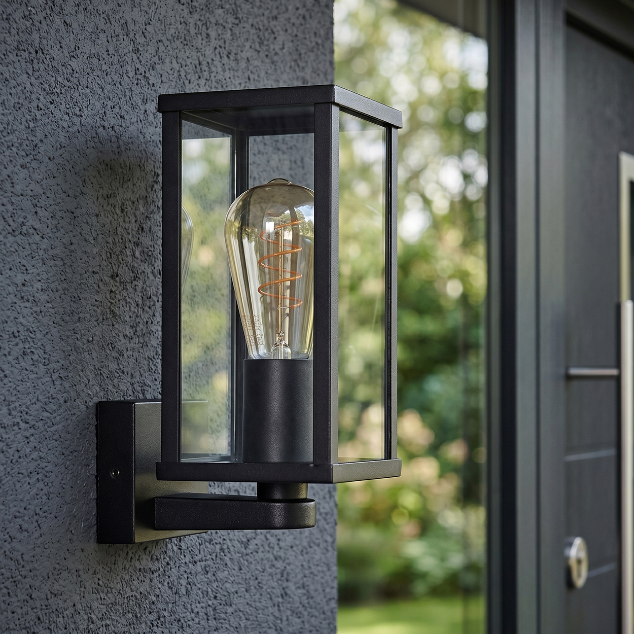 Schwarze Wandlampe mit Glasgehäuse und sichtbarer Glühbirne.