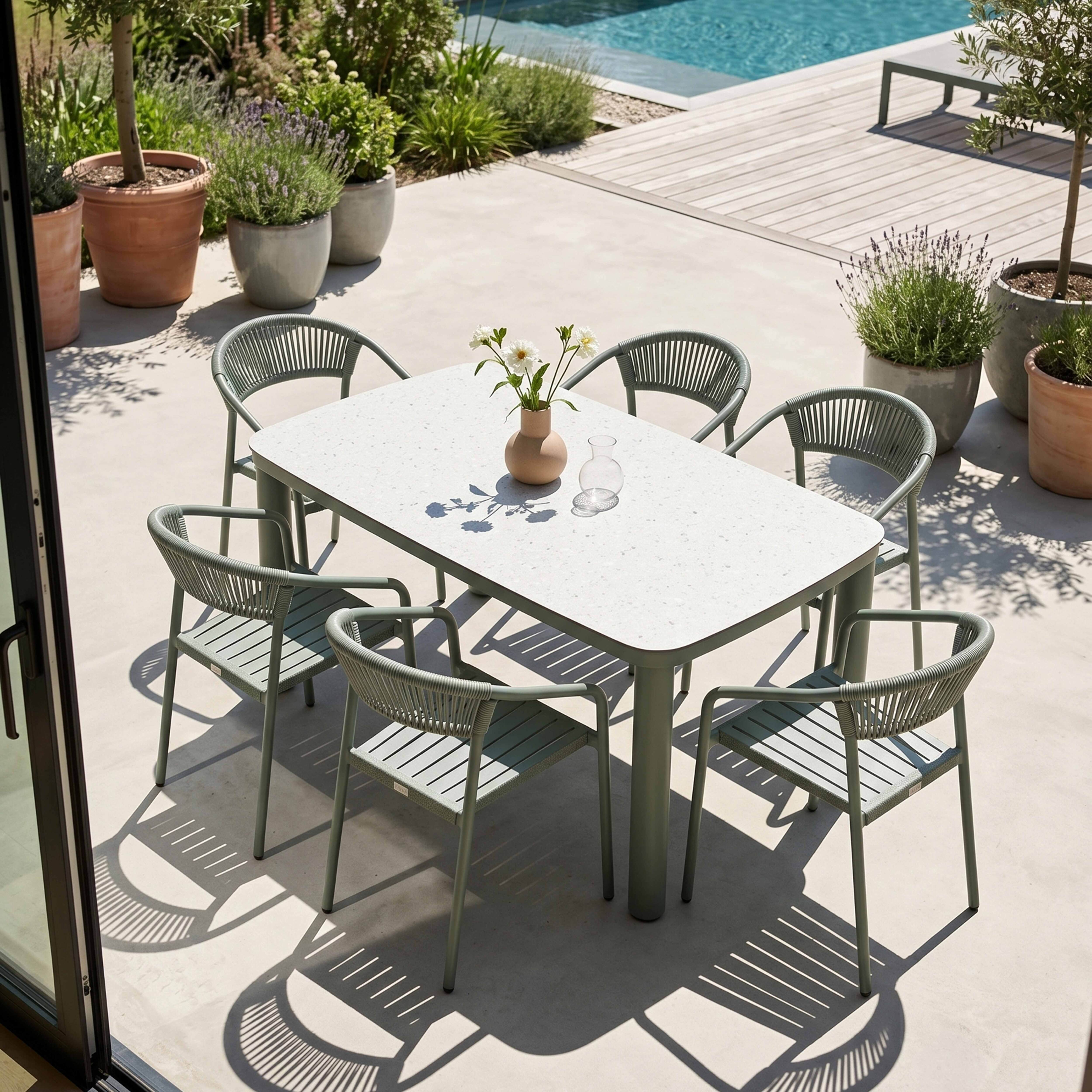 Grüne Gartenmöbel mit Tisch und Stühlen, umgeben von Pflanzen und einem Pool.