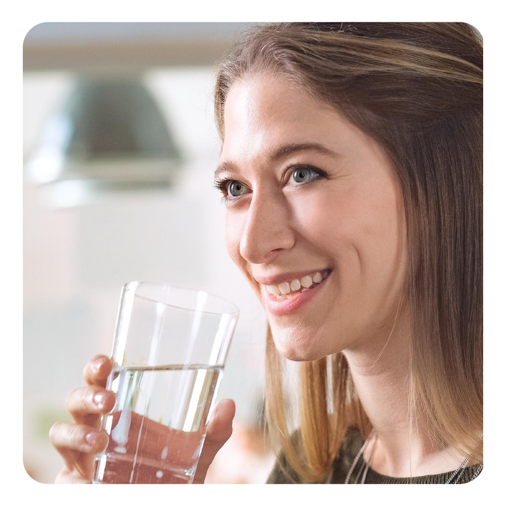 Eine Frau trinkt ein Glas Wasser und lächelt.
