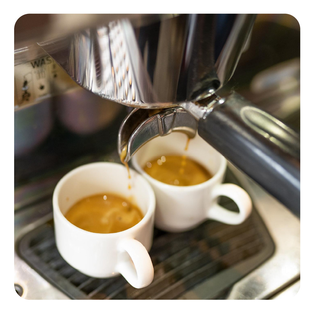 Ein Espresso fließt in zwei weiße Tassen aus einer Espressomaschine.