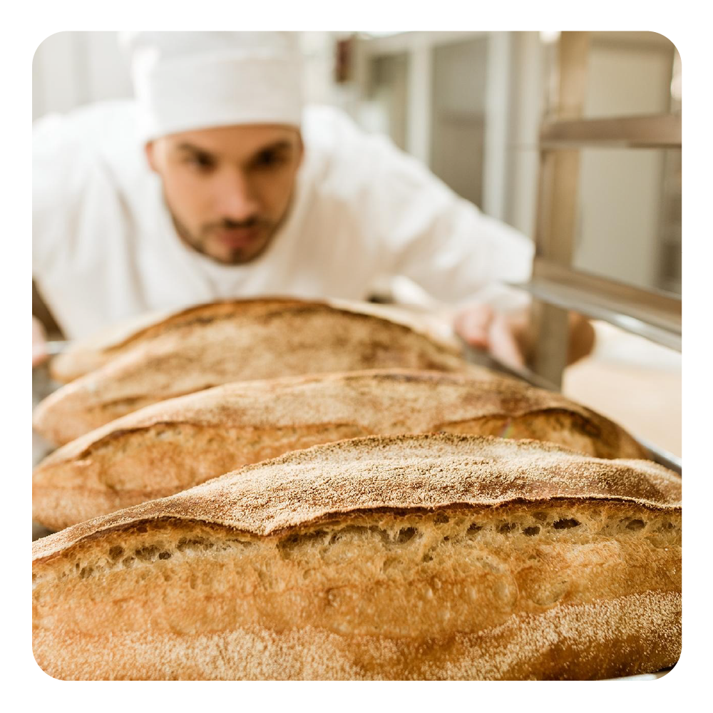 Un fornaio in uniforme bianca ispeziona pane appena sfornato su una teglia.