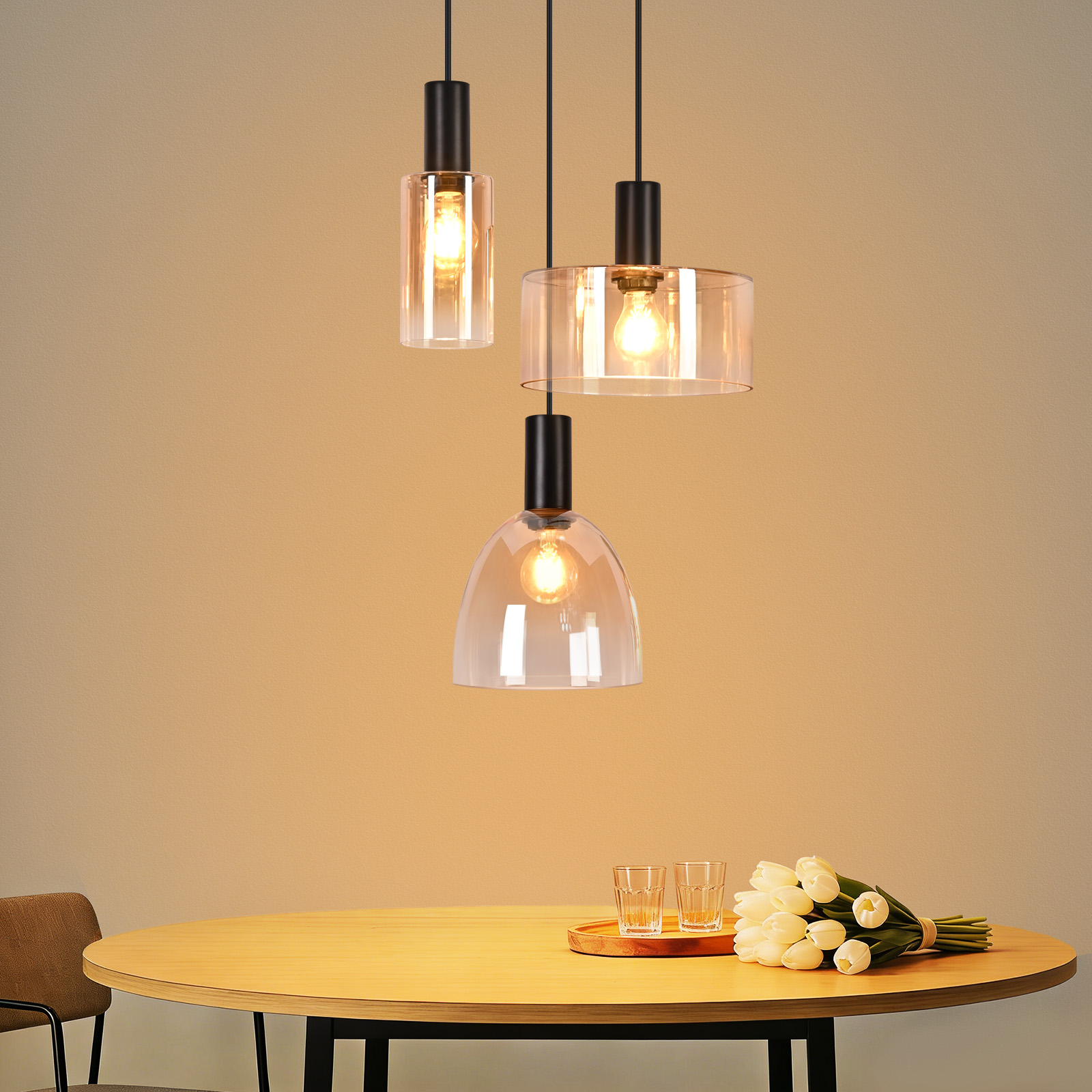 Drei Pendelleuchten mit Glaslampenschirmen über einem Holztisch mit Gläsern und Tulpen.