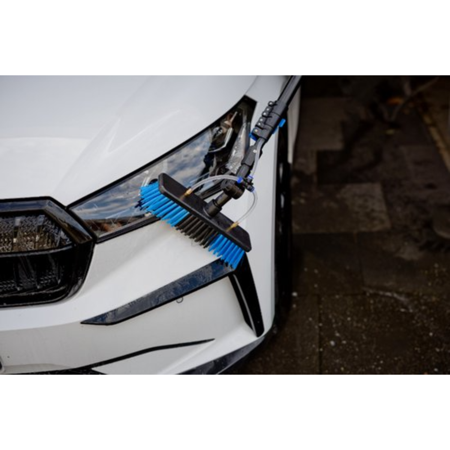 Een blauwe autowasborstel schrobt de koplamp van een witte auto.
