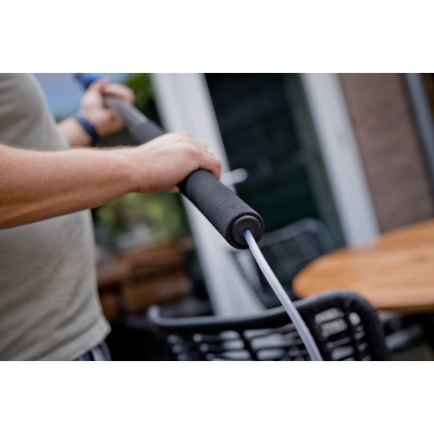 Persoon houdt zwarte handgreep met slang vast, buiten bij tafel en stoelen.
