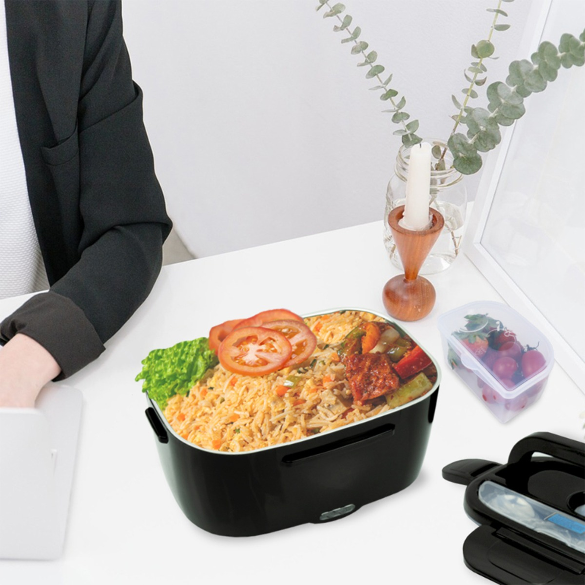 Czarna skrzynka na lunch wypełniona ryżem, warzywami i pomidorami stoi na białym biurku.