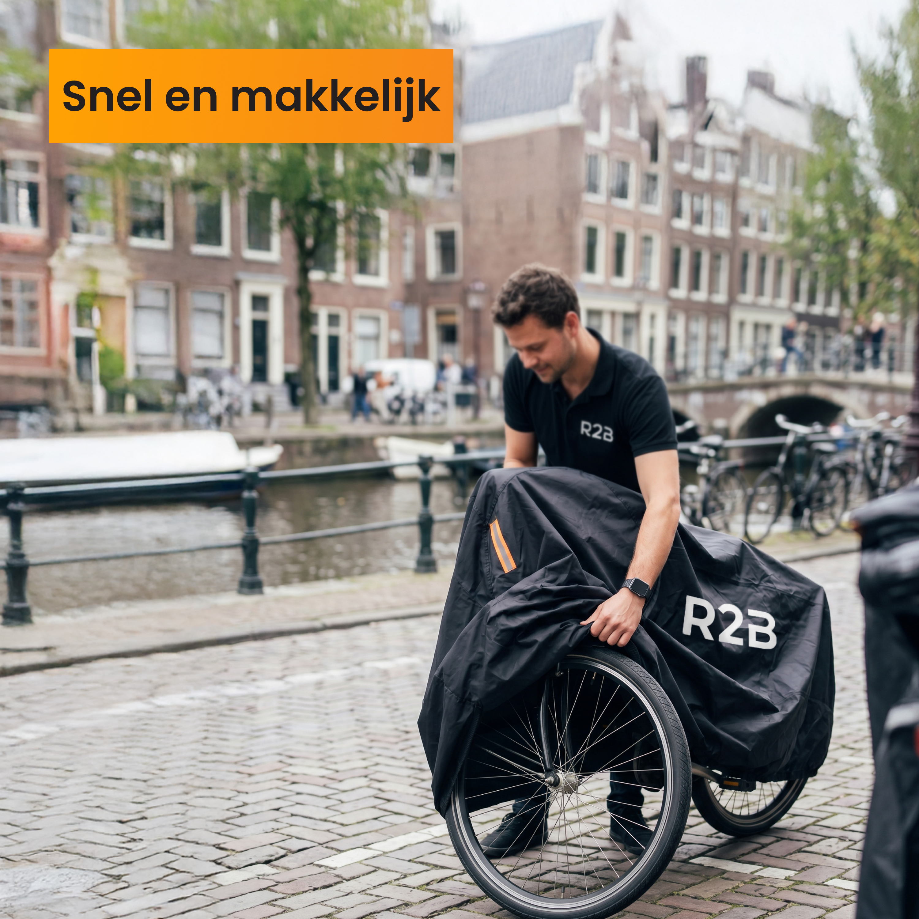 Man covers bicycle with black tarp. Amsterdam canal in background.
