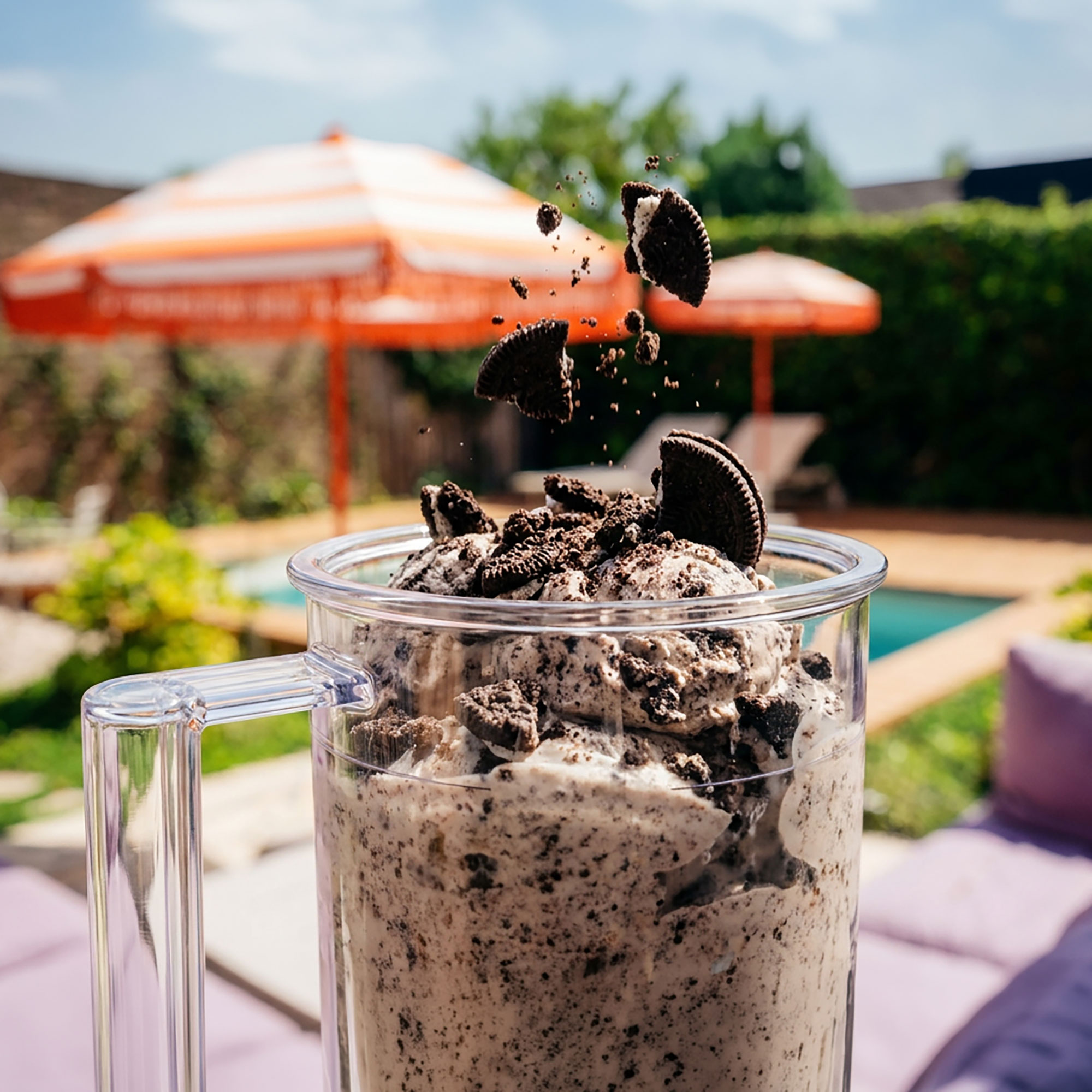 Ein Glas mit Cookies-and-Cream-Eis, Oreos fliegen herum, draußen mit Sonnenschirmen.