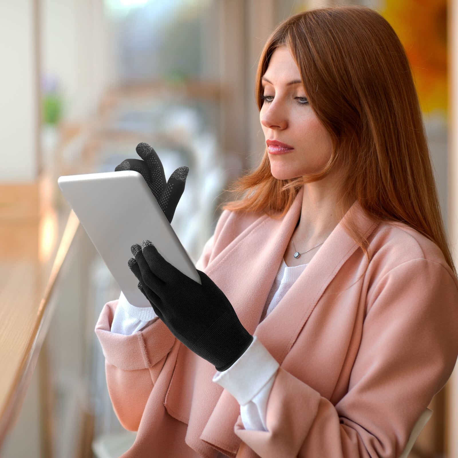 Donna con capelli rossi usa un tablet, indossa guanti neri e un cappotto rosa.
