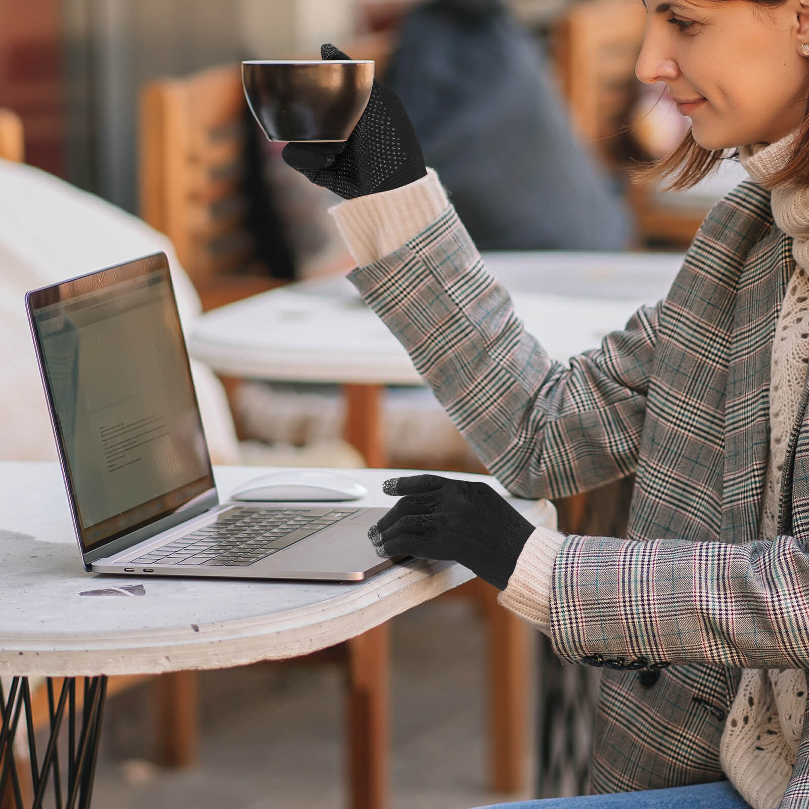 Una donna con i guanti tiene una tazza di caffè accanto a un laptop.