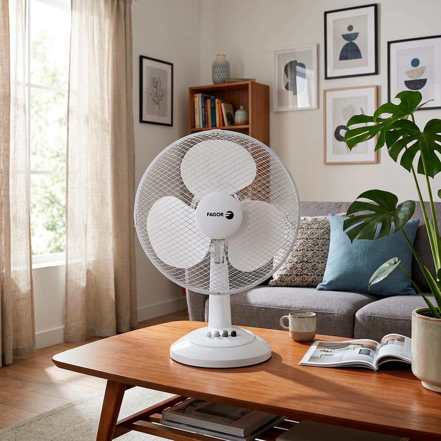 Un ventilador blanco se sienta en una mesa de madera frente a un sofá, con un libro y una taza cerca.