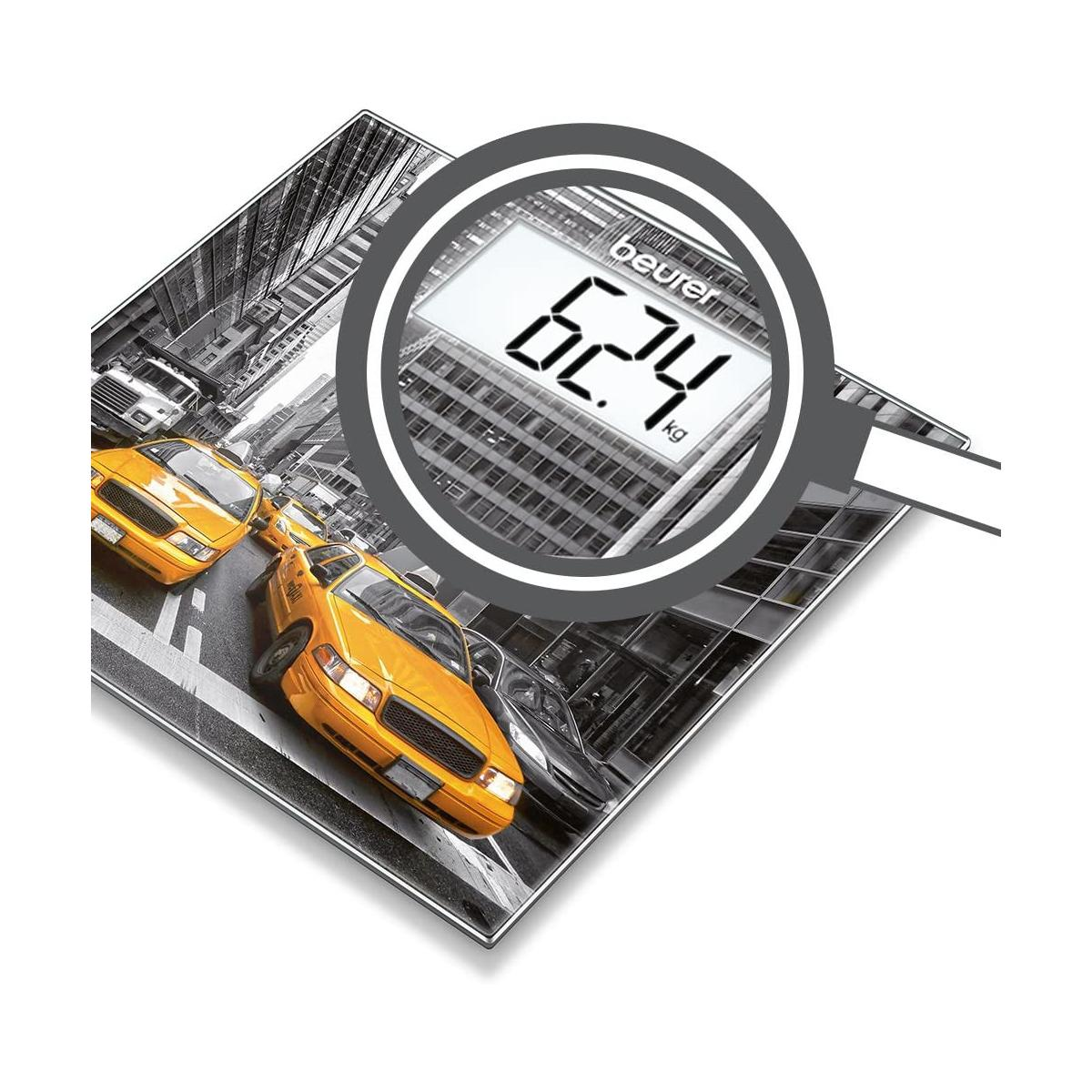 Una báscula con una calle de la ciudad, taxis amarillos y rascacielos. Pantalla digital muestra 62,4 kg.