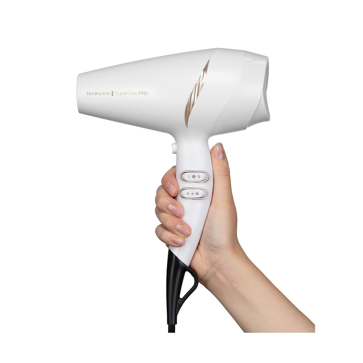 Een hand houdt een witte Remington haardroger met gouden accenten vast.