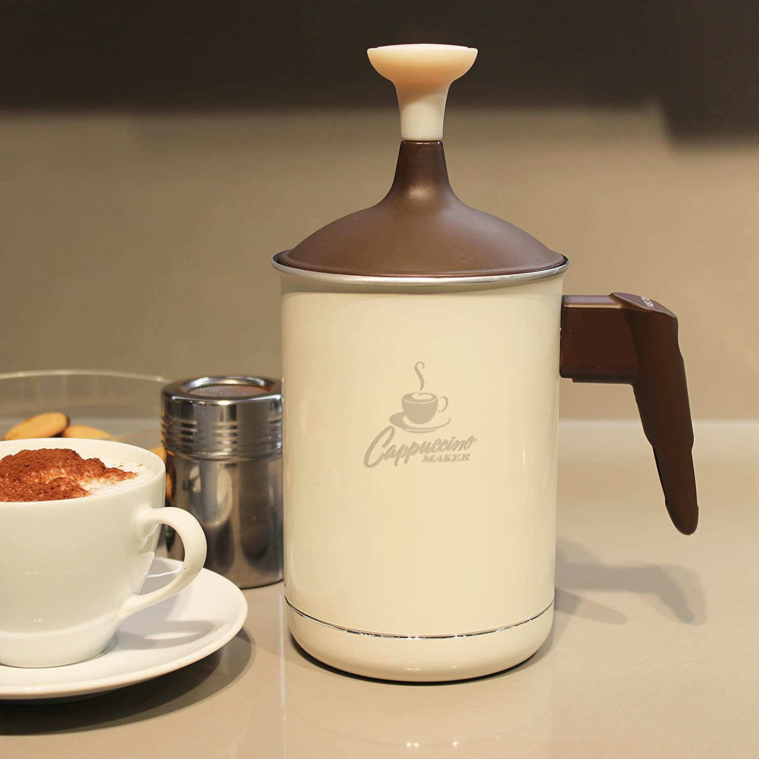 Una montalatte color crema con accenti marroni, accanto a una tazza di caffè.