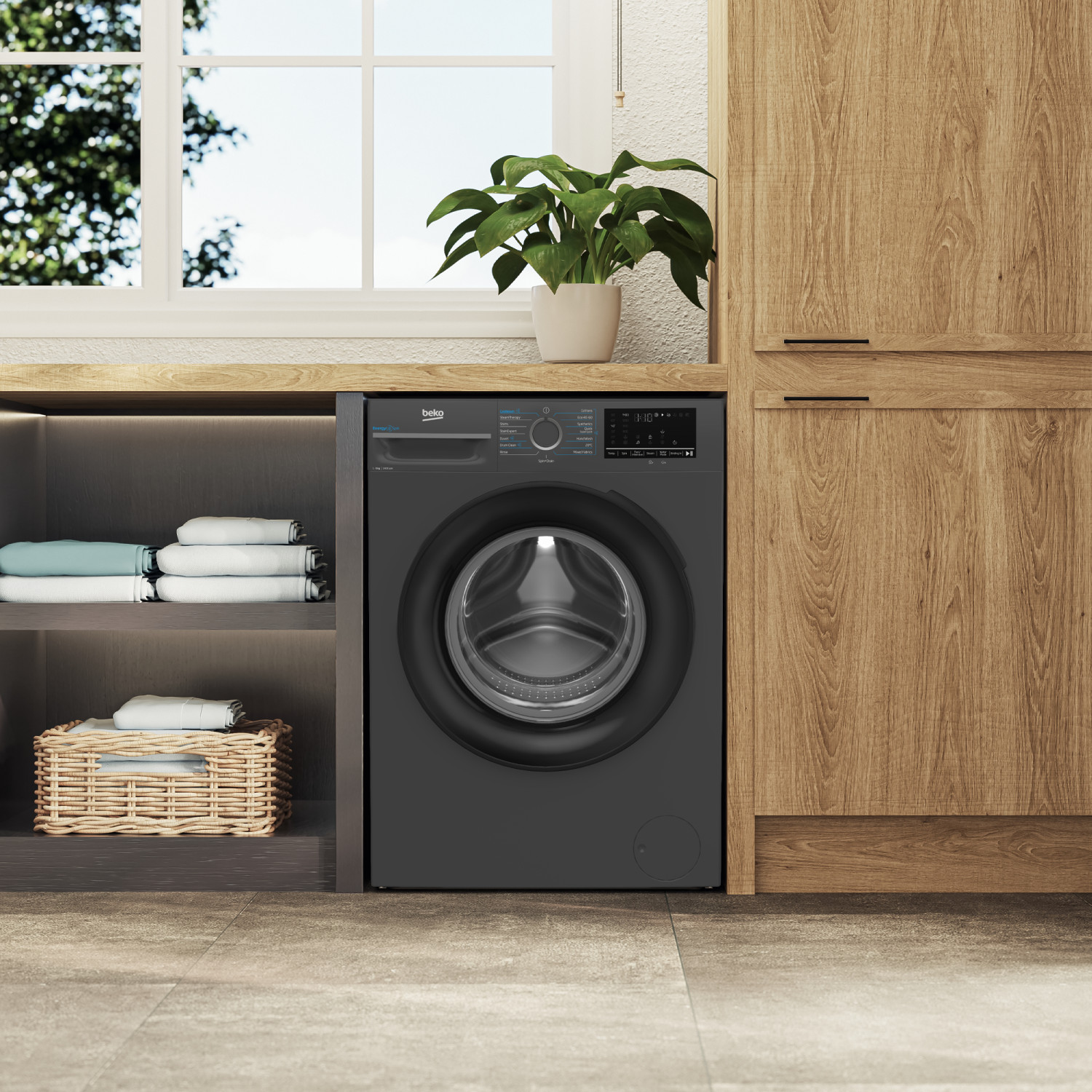 Una lavatrice Beko grigio scuro accanto ad armadi in legno. Asciugamani piegati su una mensola e in un cesto.