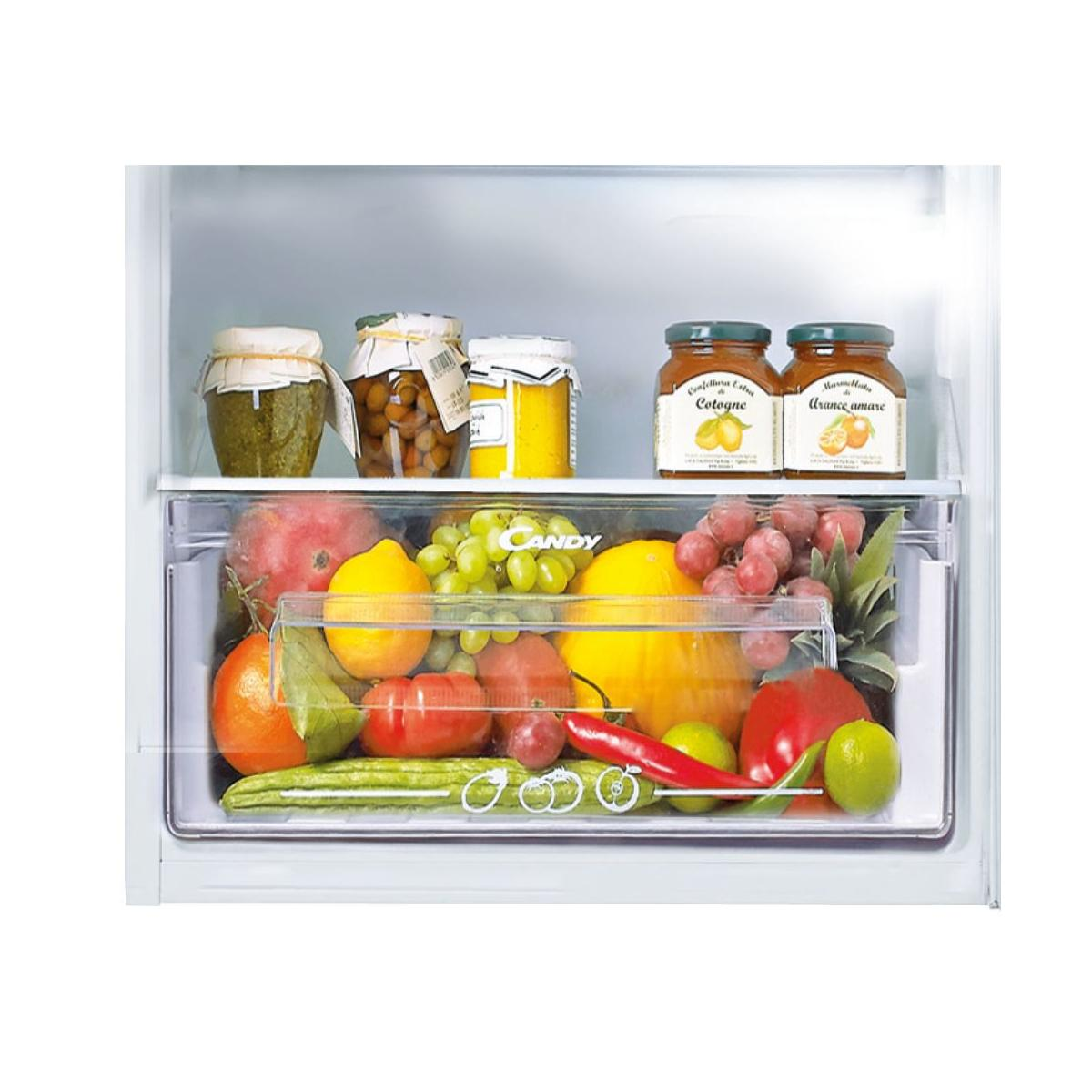 Un cassetto del frigorifero pieno di frutta e verdura: mango, limoni, uva, melone, pomodori, cetrioli, peperoni, peperoncini, arance.