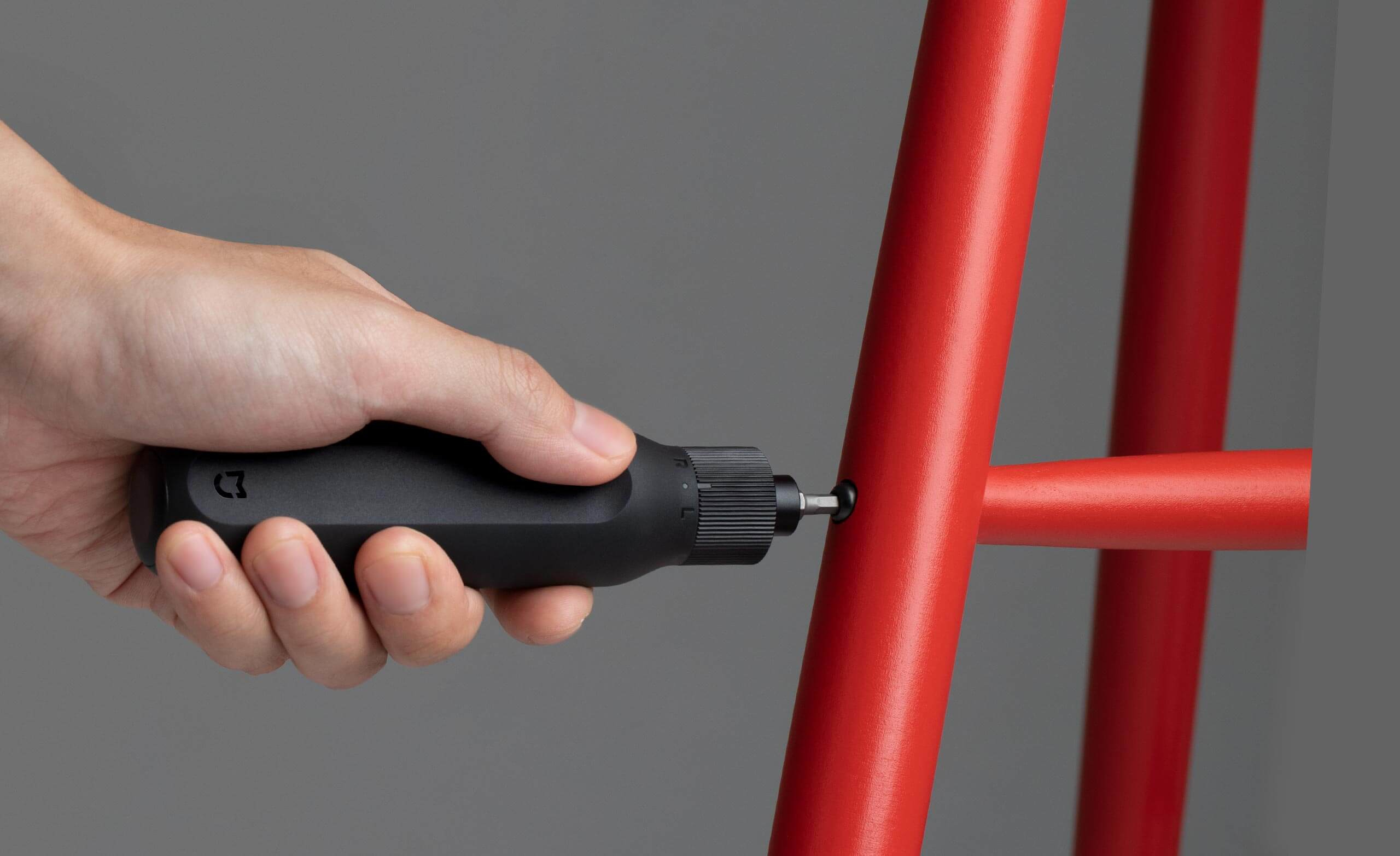 Una mano usa un destornillador negro para sujetar un soporte de silla rojo.