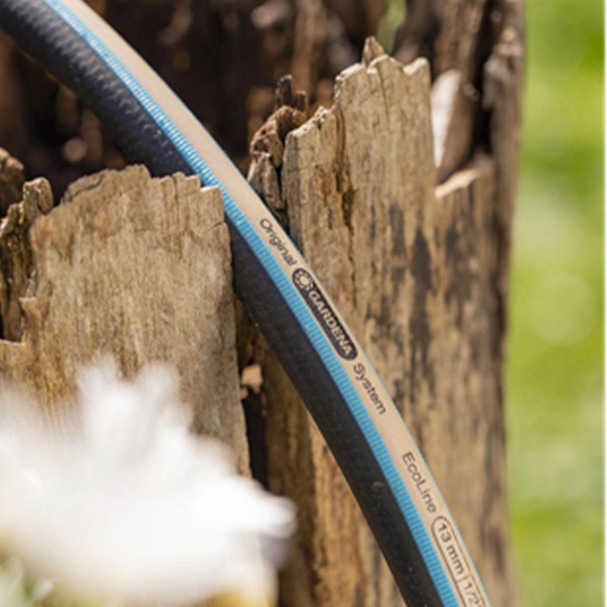 Un tubo da giardino con logo Gardena appoggiato su un ceppo.
