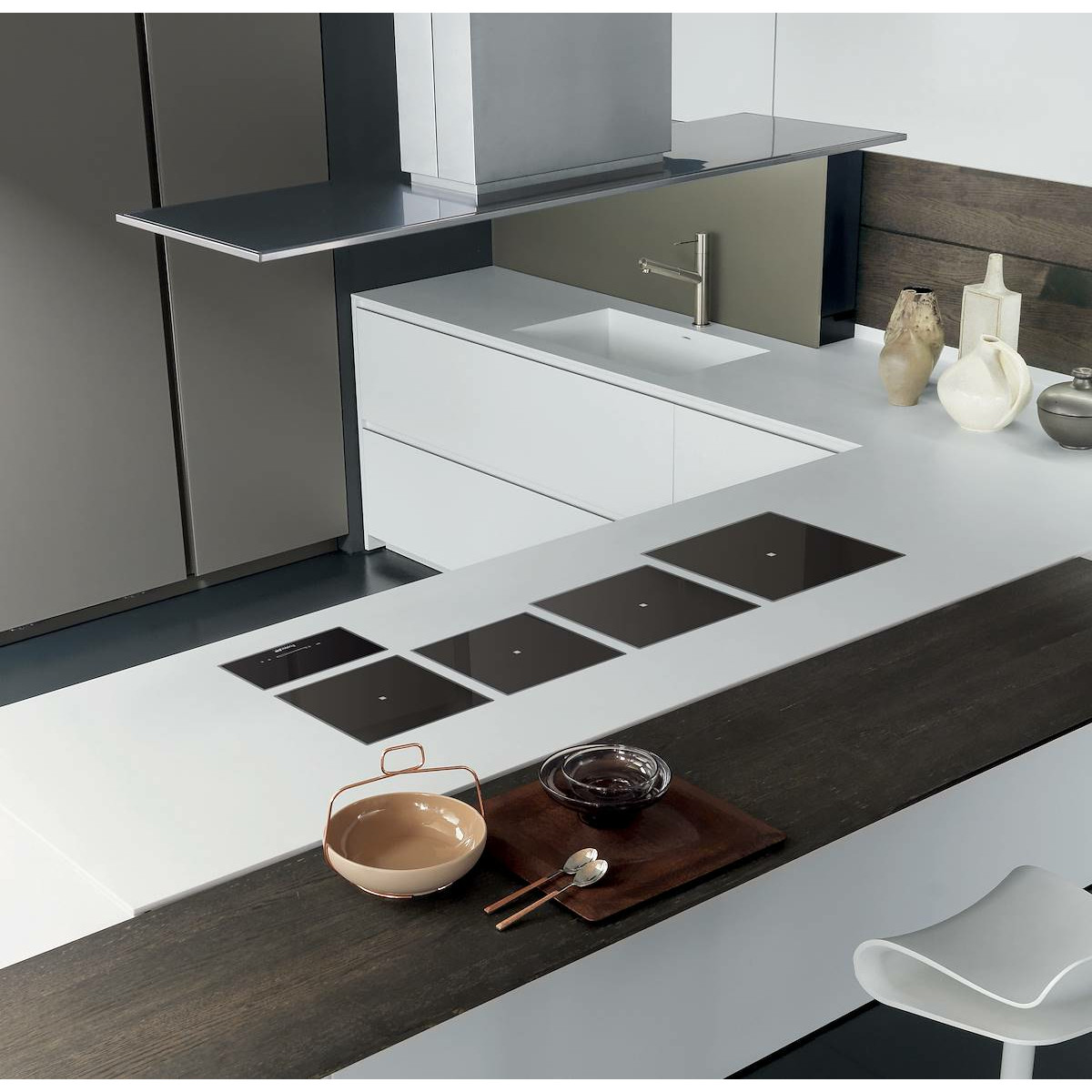 Cucina moderna con piani di lavoro bianchi, piani cottura a induzione e cappa argento.