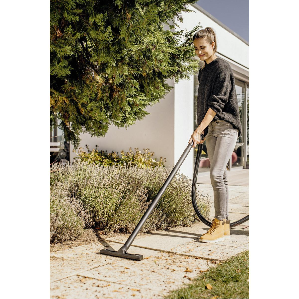 Woman vacuums patio in front of house next to lavender and tree.