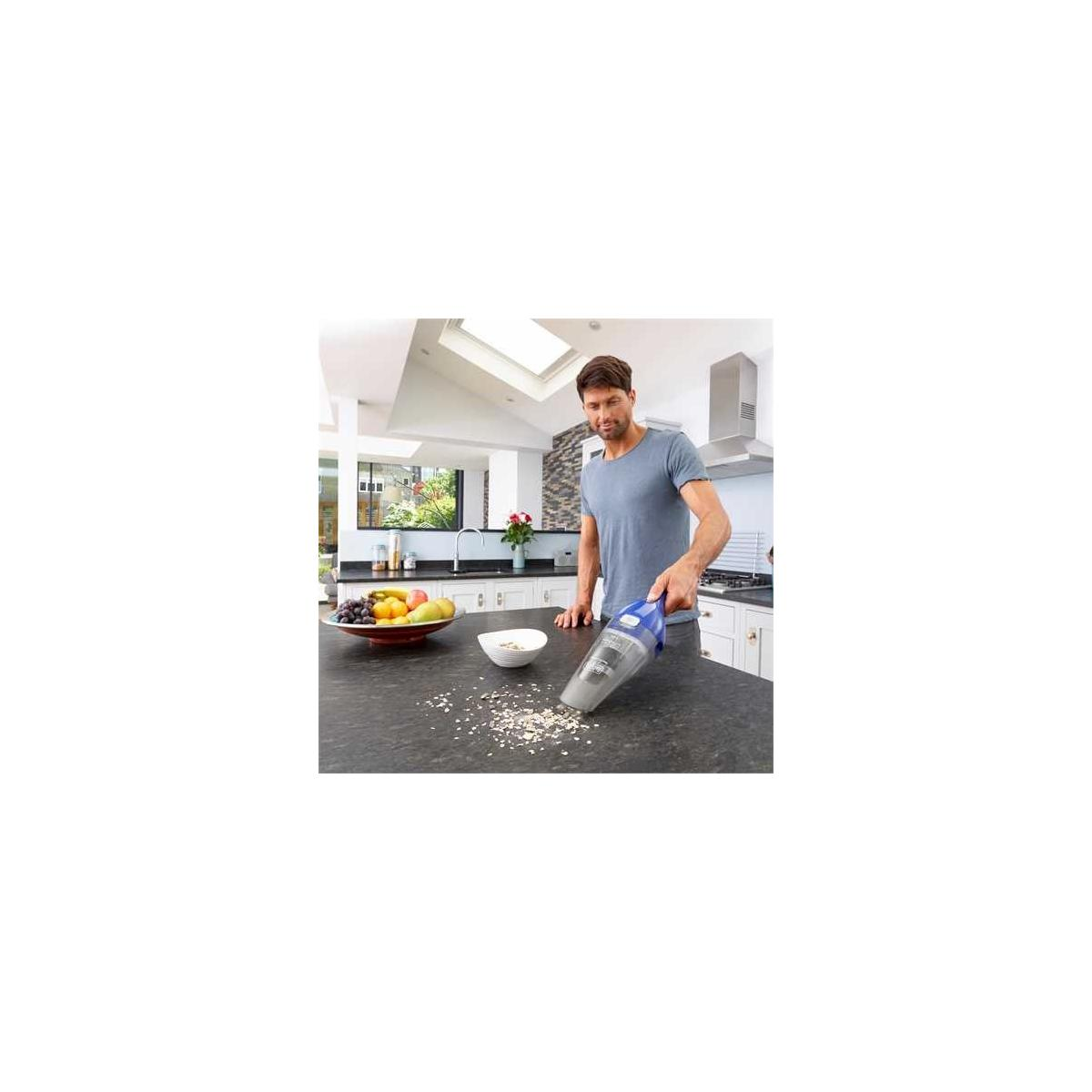 Un hombre usa una aspiradora de mano para limpiar migas de una encimera de cocina.