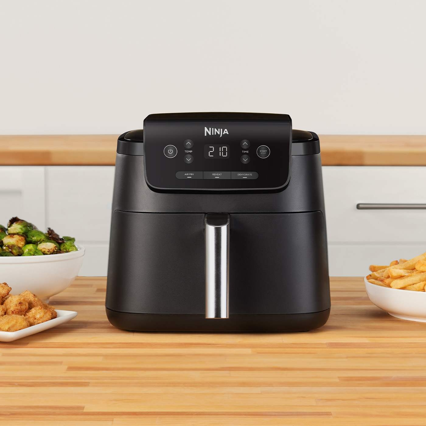 Friteuse à air Ninja noire avec commandes numériques, à côté de bols de nourriture.