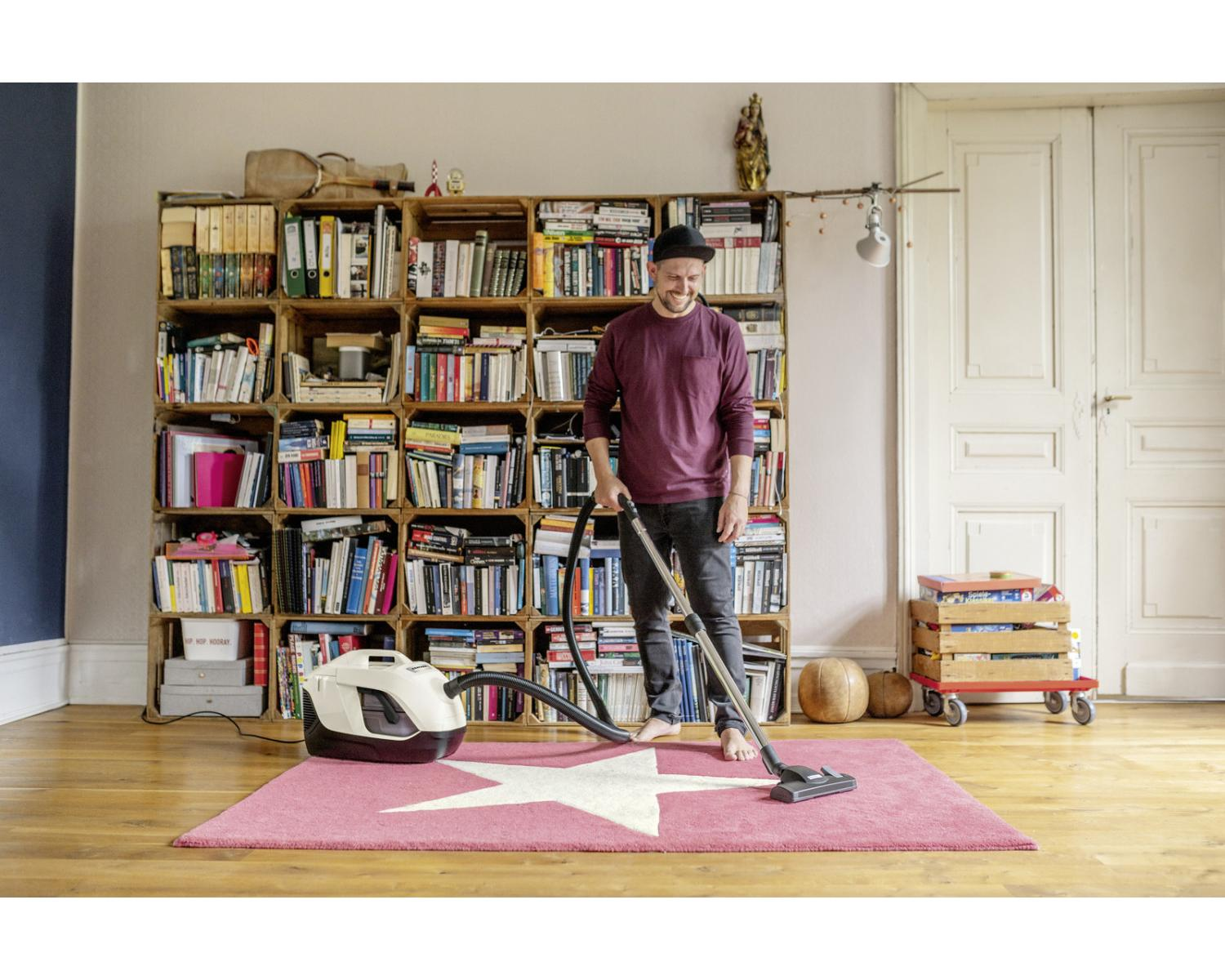 Un homme passe l'aspirateur sur un tapis étoilé. Bibliothèque derrière.