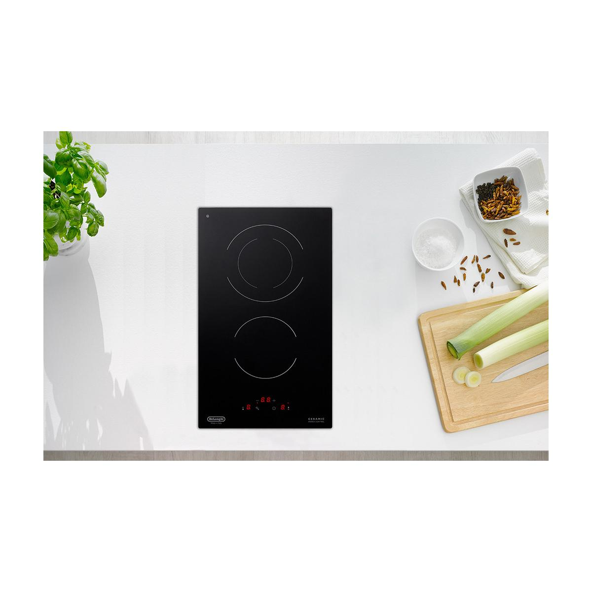 Un piano cottura in vetroceramica nero con due zone, accanto agli ingredienti.