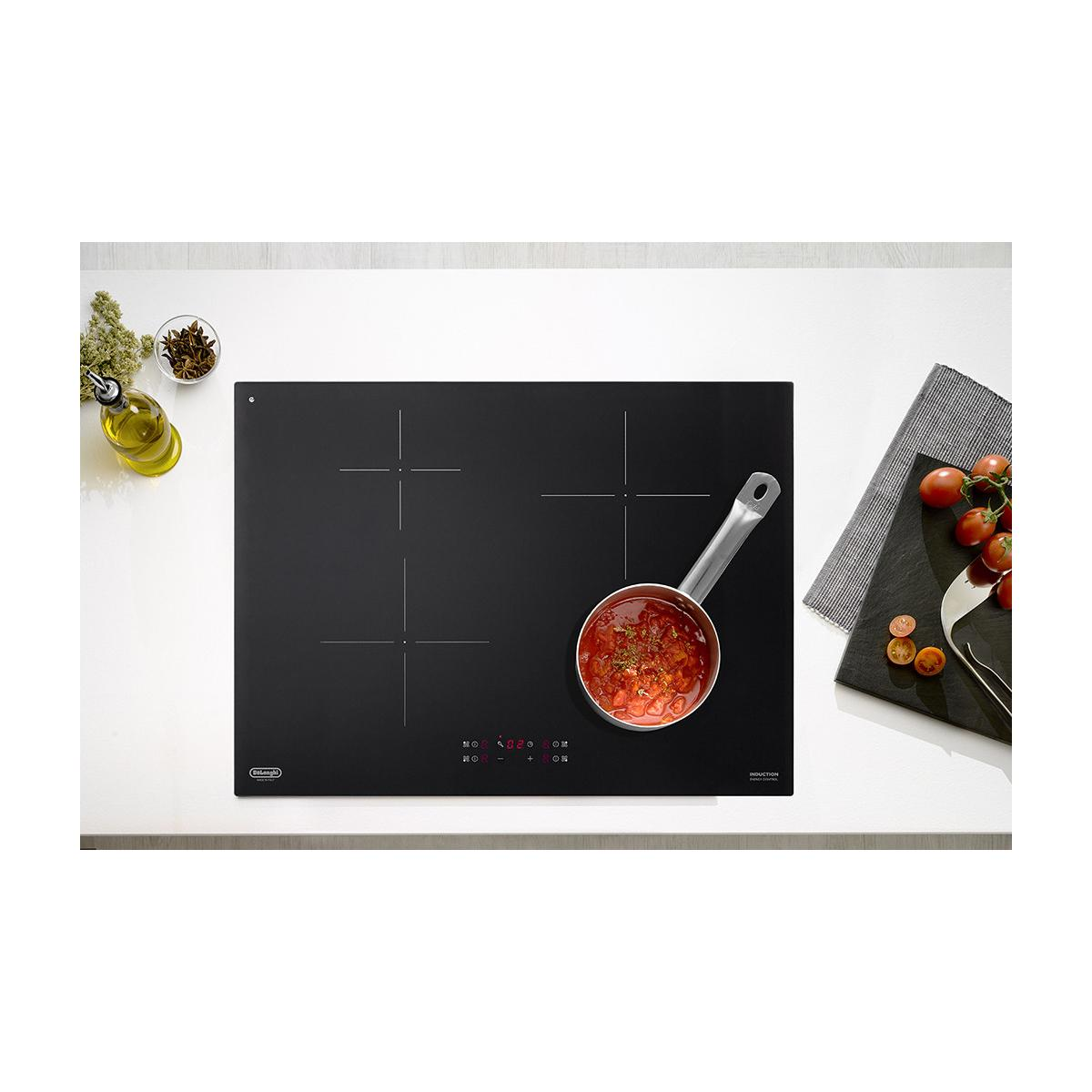 Placa de inducción negra con olla, aceite de oliva y tomates.