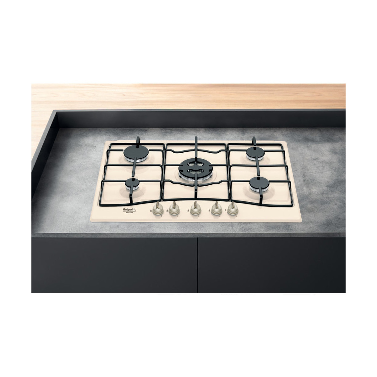 Una placa de gas color crema con cuatro quemadores y perillas plateadas sobre una encimera de hormigón.