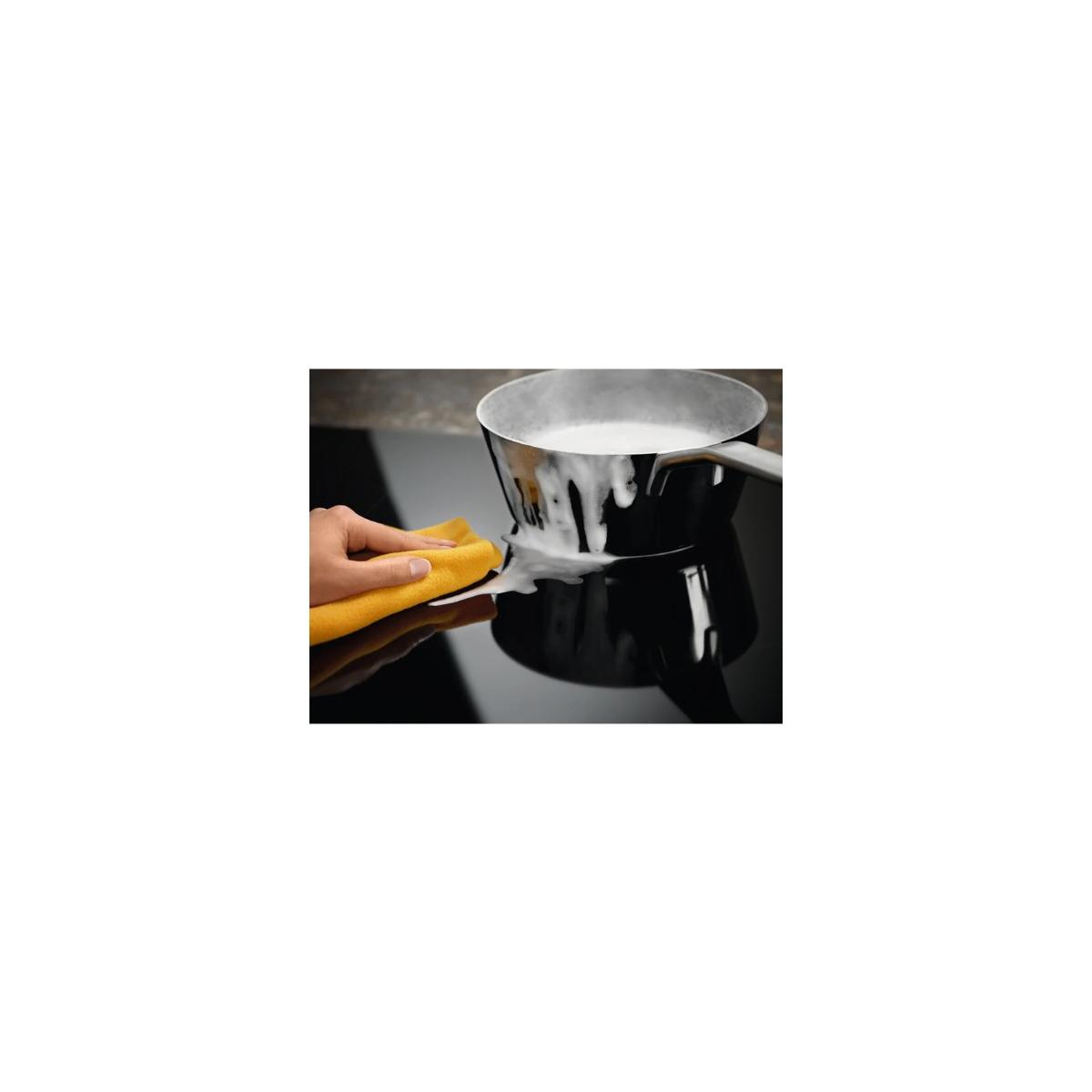 Een hand maakt een pan schoon op een zwart fornuis met een gele doek.