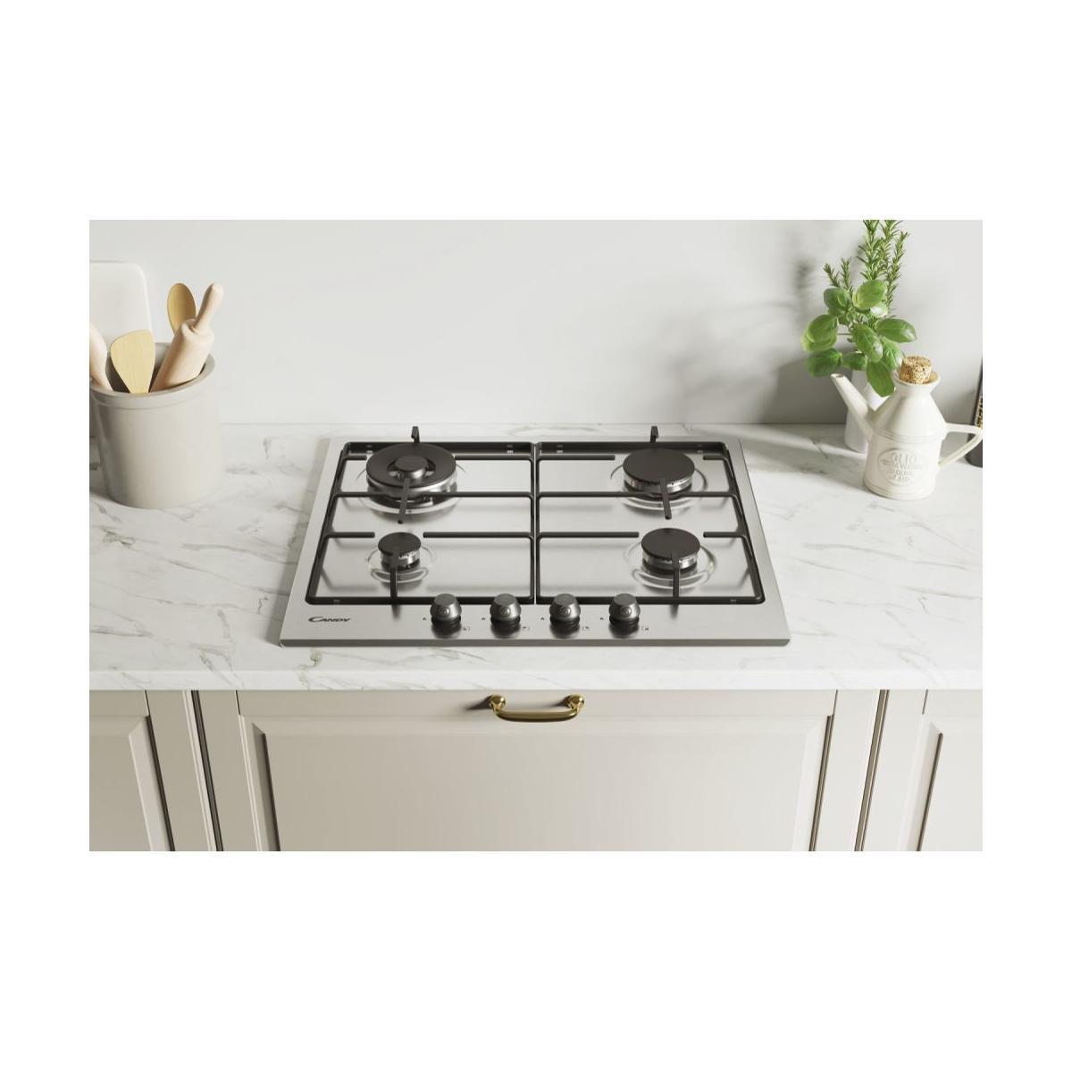 Piano cottura a gas in acciaio inox con quattro fuochi su top in marmo. Utensili in cucina sullo sfondo.