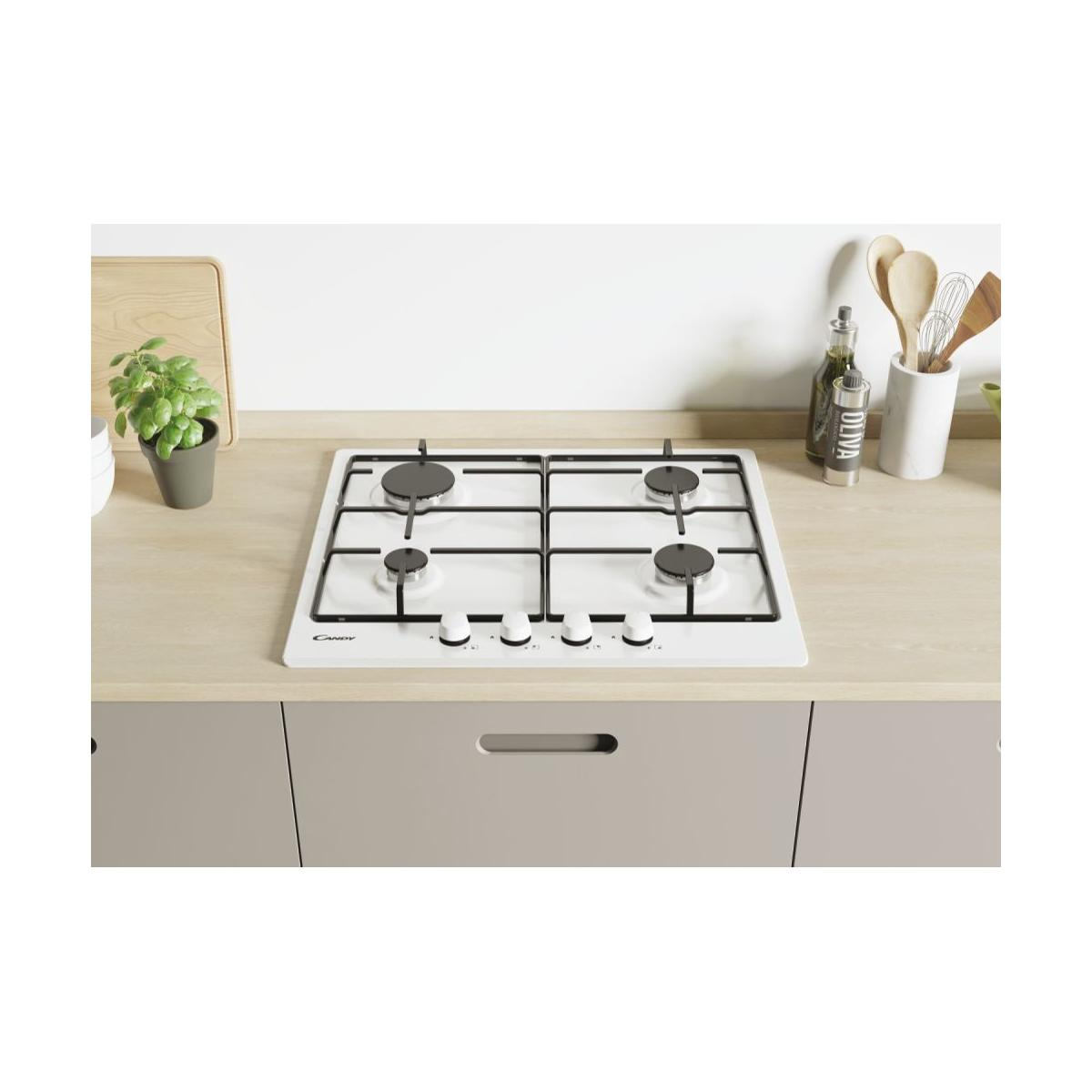 Un piano cottura a gas bianco a quattro fuochi su piano di lavoro in legno, con utensili.