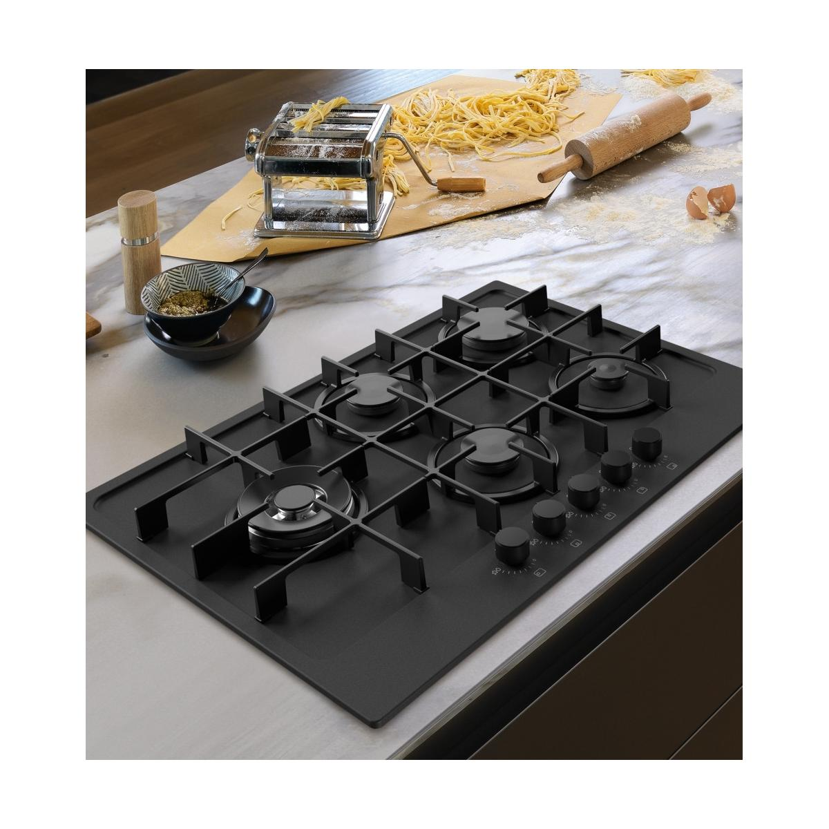 Piano cottura a gas nero con macchina per pasta, pasta, mattarello e uova.