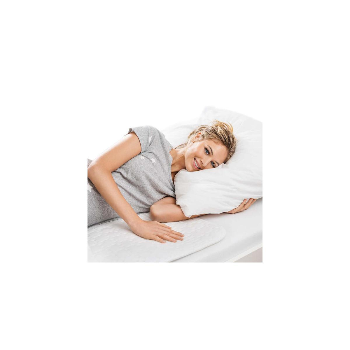Eine Frau liegt auf einem Bett mit einem Kissen und einem weißen Pad.
