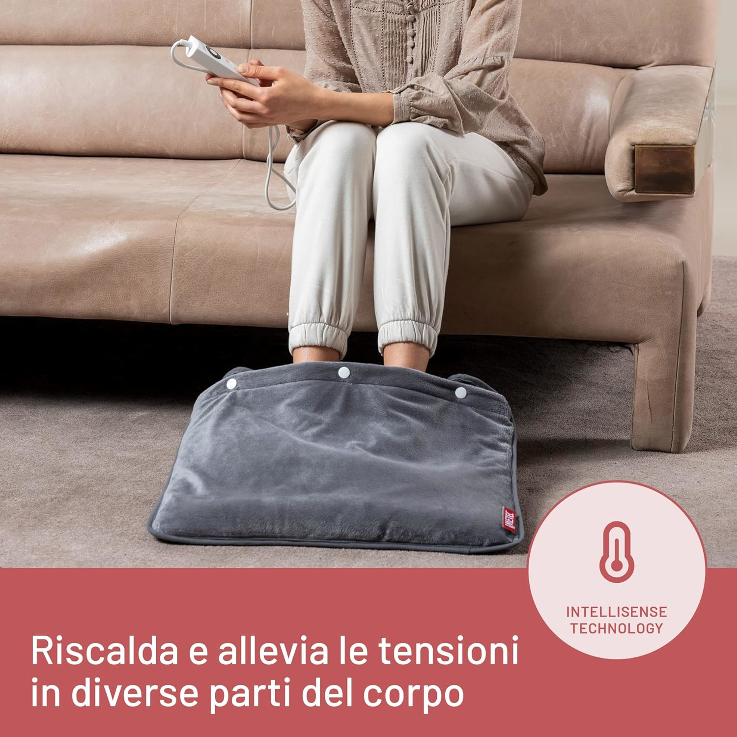 Una persona seduta su un divano usa una coperta termica per i piedi.