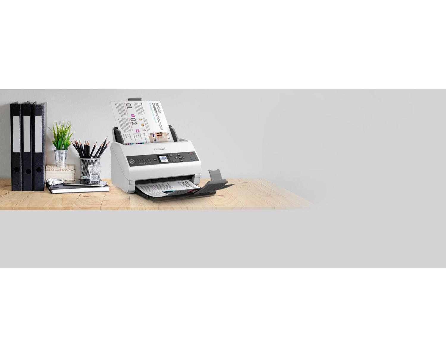 Ein weißer Scanner auf einem Holztisch mit Aktenordnern und Stiften daneben.