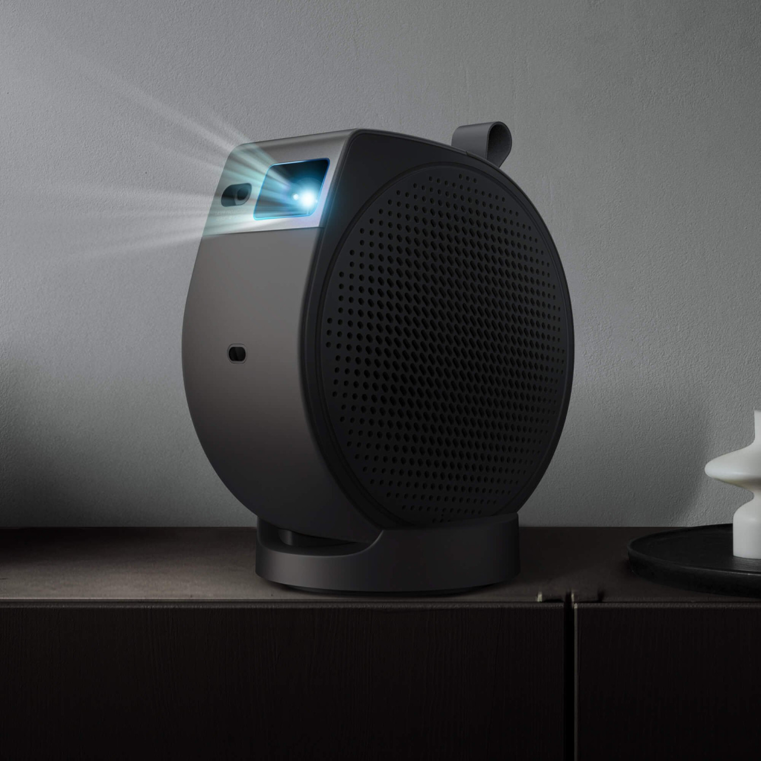 Un projecteur noir avec une lentille lumineuse sur une étagère sombre.