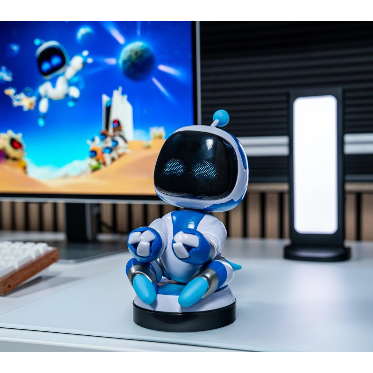 Ein kleiner blauer und weißer Roboter sitzt auf einem Schreibtisch vor einem Monitor.