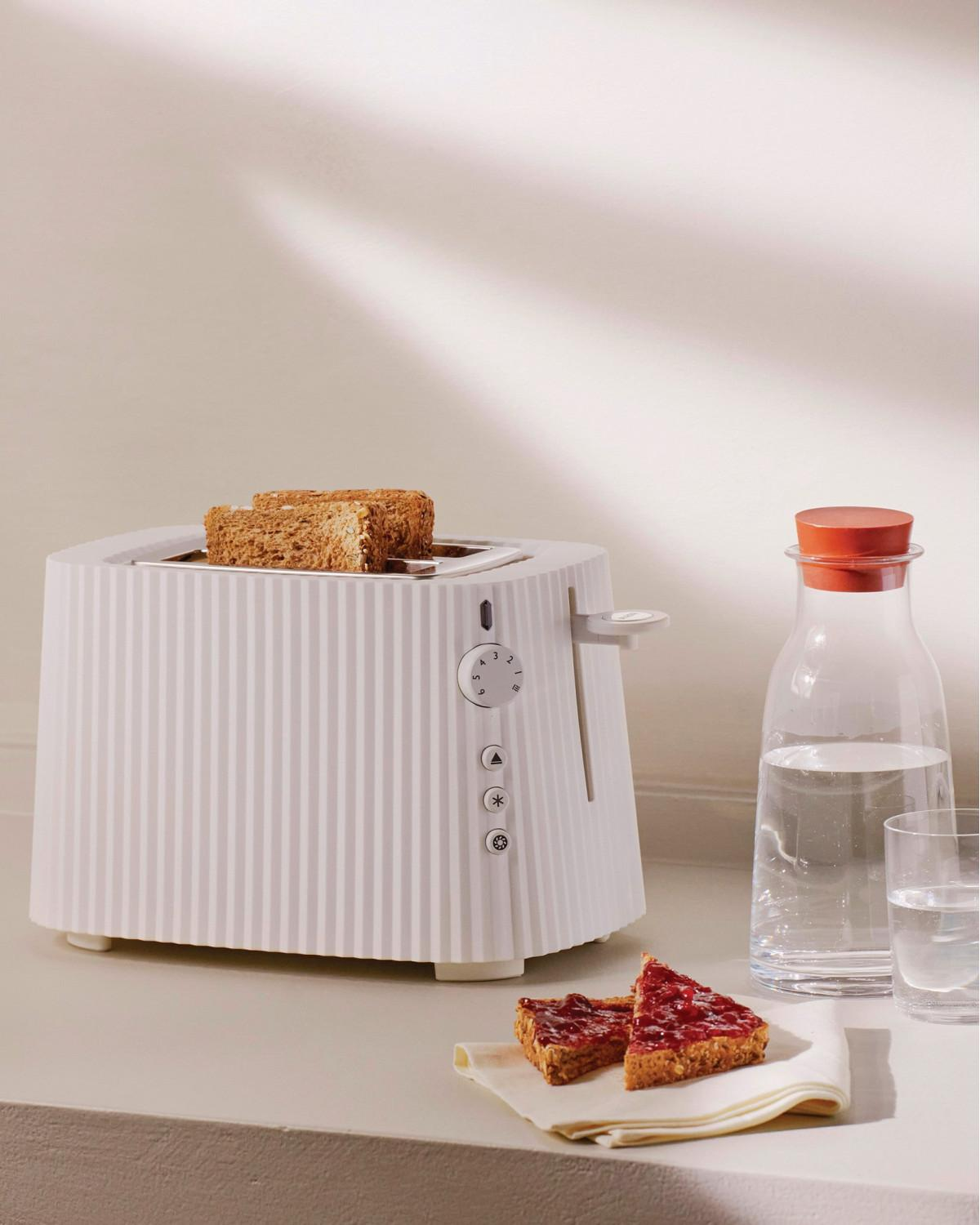 Ein weißer Toaster mit zwei Scheiben Toast, daneben ein Glas Wasser und Marmeladenbrot.